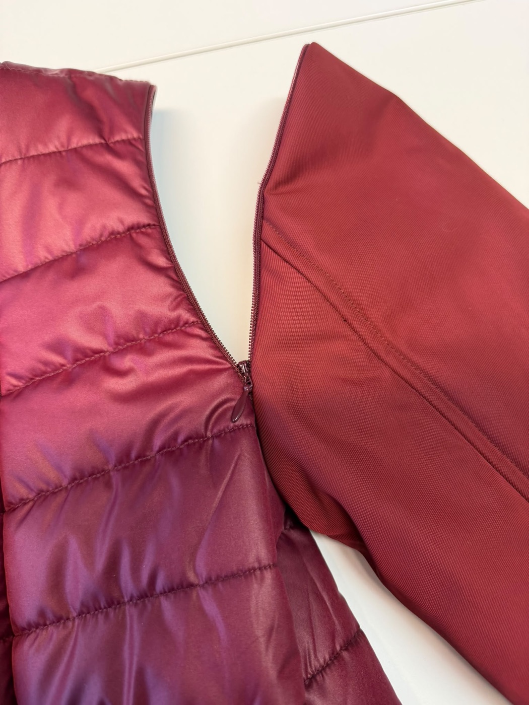 Dettaglio della cerniera invisibile Modular Wear: pannello trapuntato bordeaux e pannello drill opaco separati, zip semi-aperta nel bordo